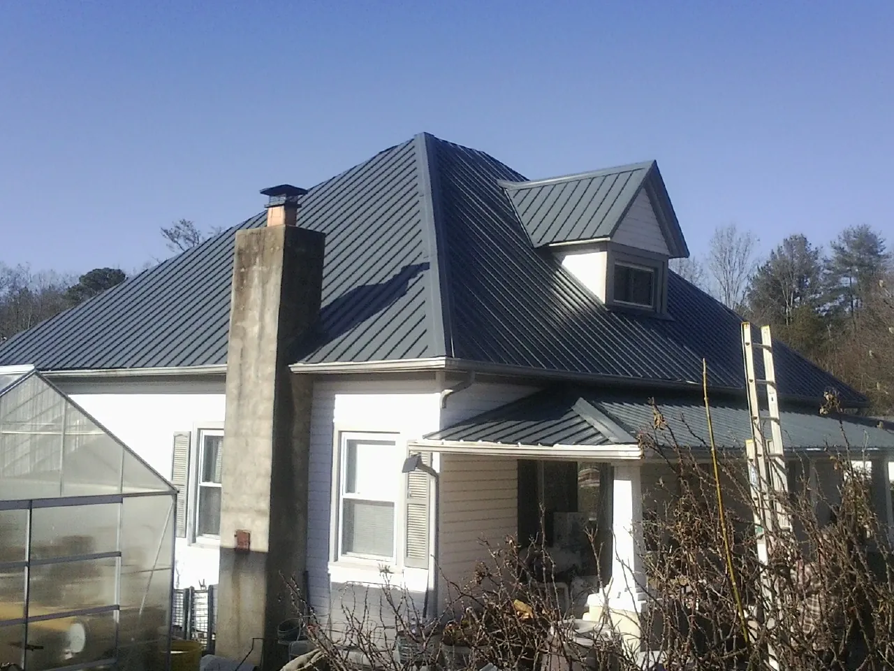Dark blue standing seam metal roof on a white farmhouse with dormer — Slate & Tile Roof Repair by Roofing Brothers in West Concord