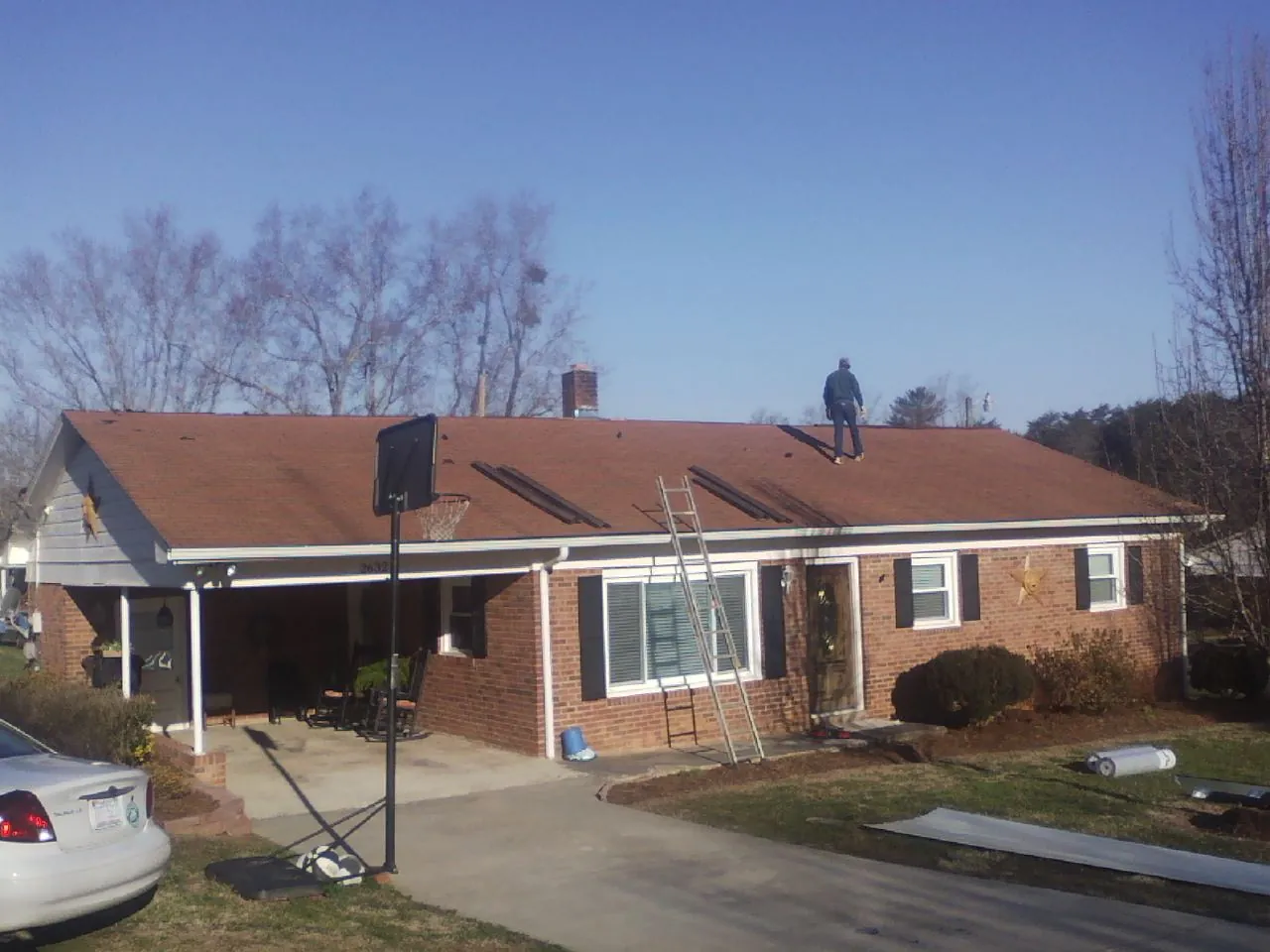 Roofer stripping a shingle roof on a brick ranch before metal panels in West Concord