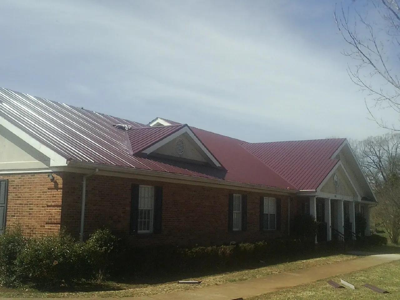 Red metal roof with gabled entries on a long brick building, from a Hail Damage Roof Repair job in West Concord