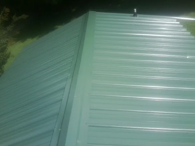 New green metal panels meeting at the ridge of a roof — Flat Roof Repair work by our crew in West Concord