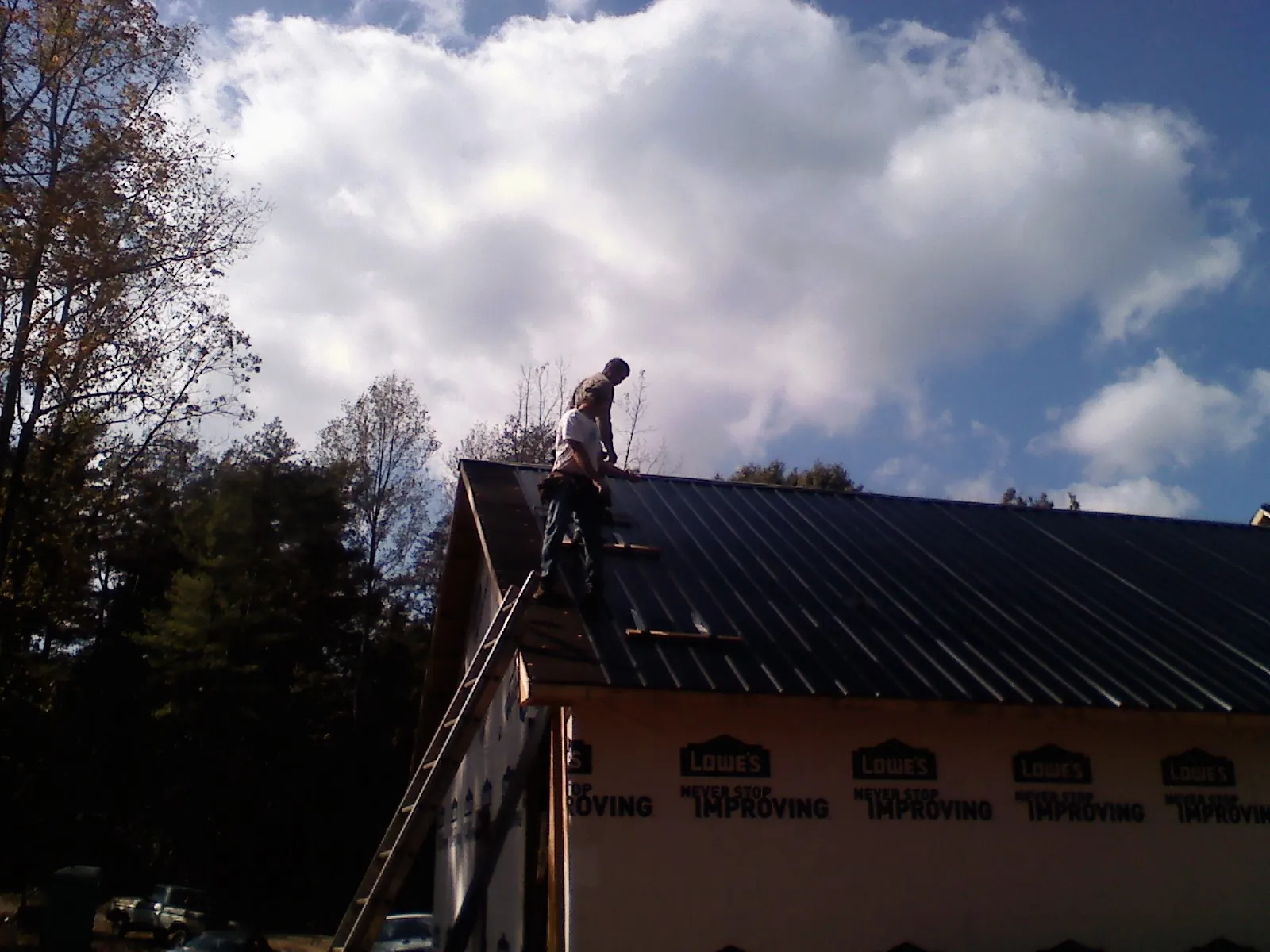 Roofer fastening dark metal panels high against a cloudy sky, from a Roof Inspection job in West Concord