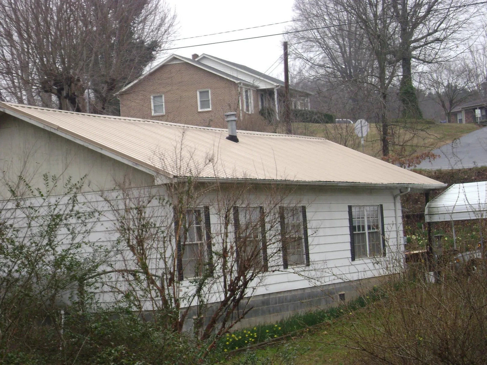 Tan metal roof on a white sided house set into a hillside — Commercial Roofing by Roofing Brothers in West Concord